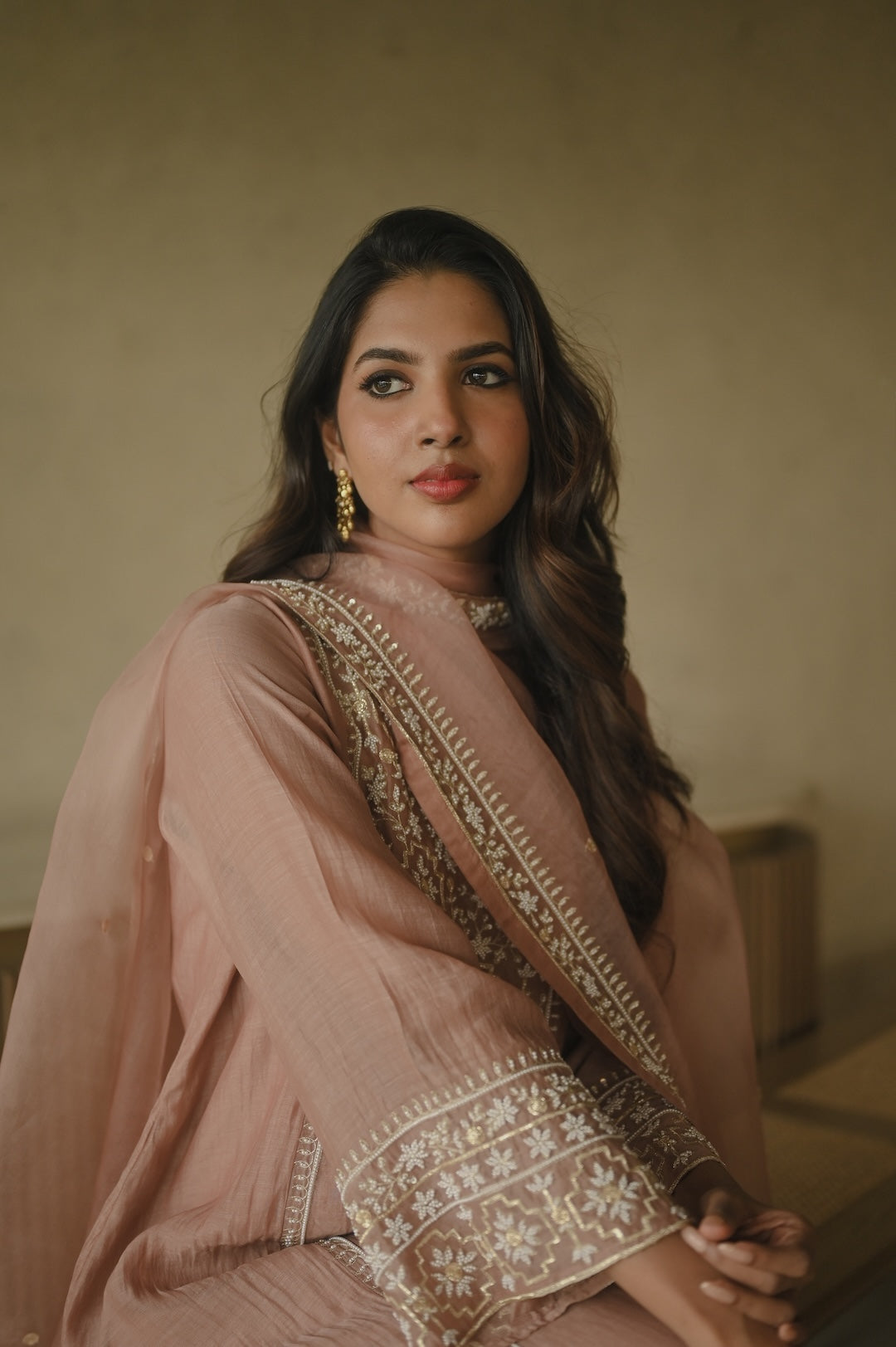 Woman wearing a traditional outfit with intricate patterns against a neutral background